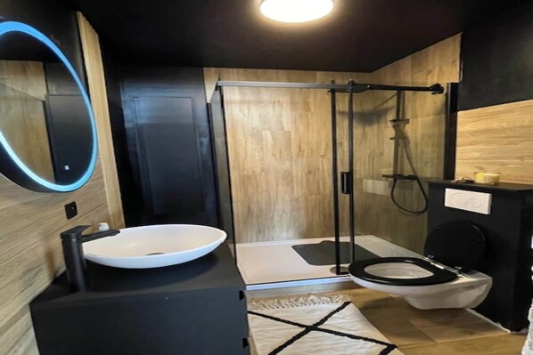 A modern bathroom with a black sink, white toilet, and a glass shower enclosure.