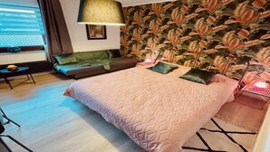 Une chambre à coucher comprenant un lit, un canapé, une lampe et un mur orné d’un motif de feuilles.