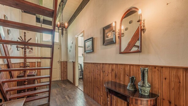 A wooden-paneled hallway with a wooden staircase, a mirror, and a small table with decorative items.