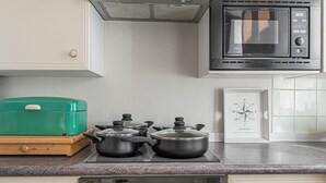 A kitchen with a stove, pots, a microwave, and a green appliance on the counter.