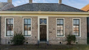 A brick building with a tiled roof, a central entrance with a door, and a small porch area.