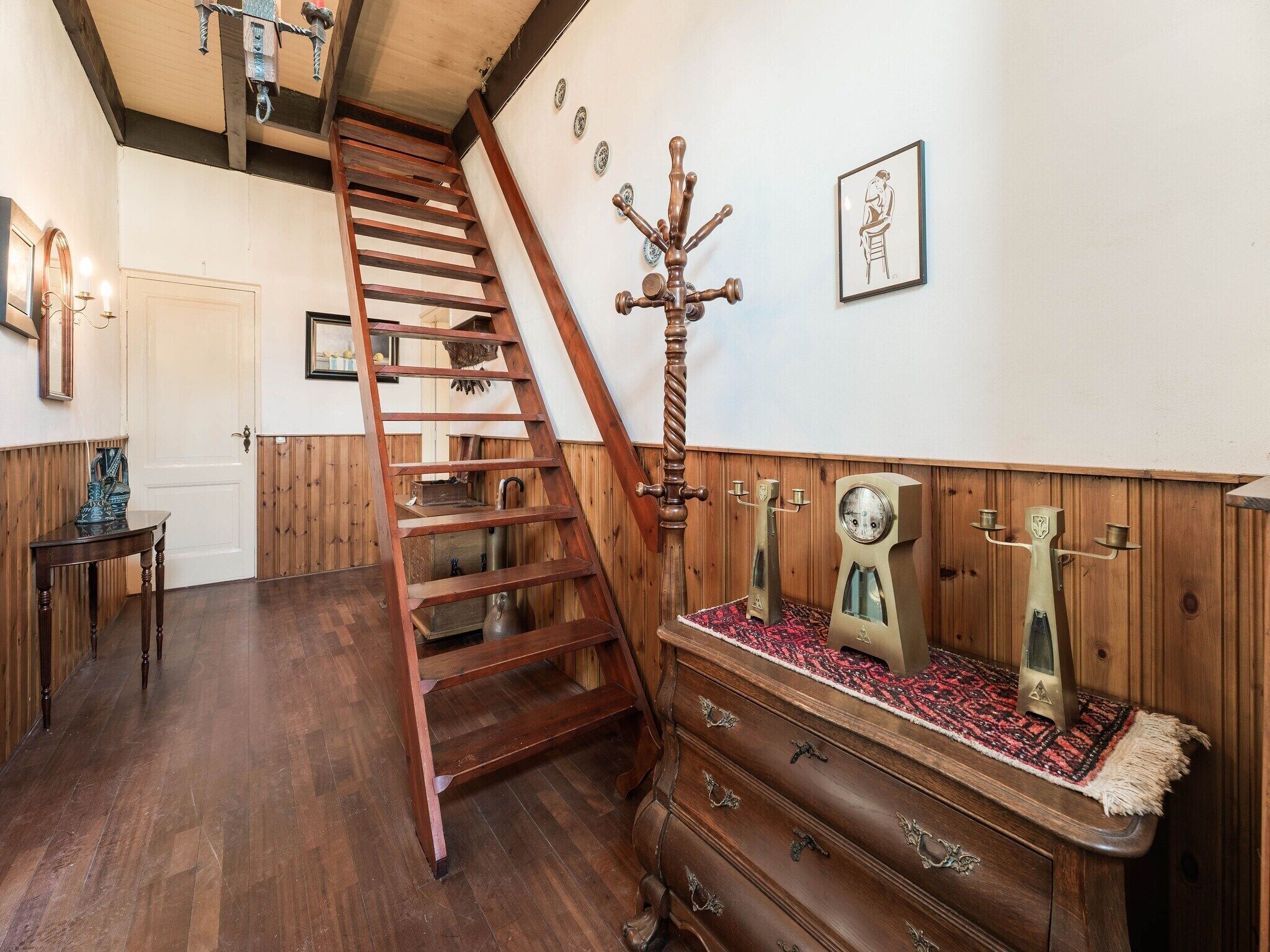 Una escalera de madera con barandilla metálica, un aparador de madera con cajones y un perchero de pared con varios ganchos.