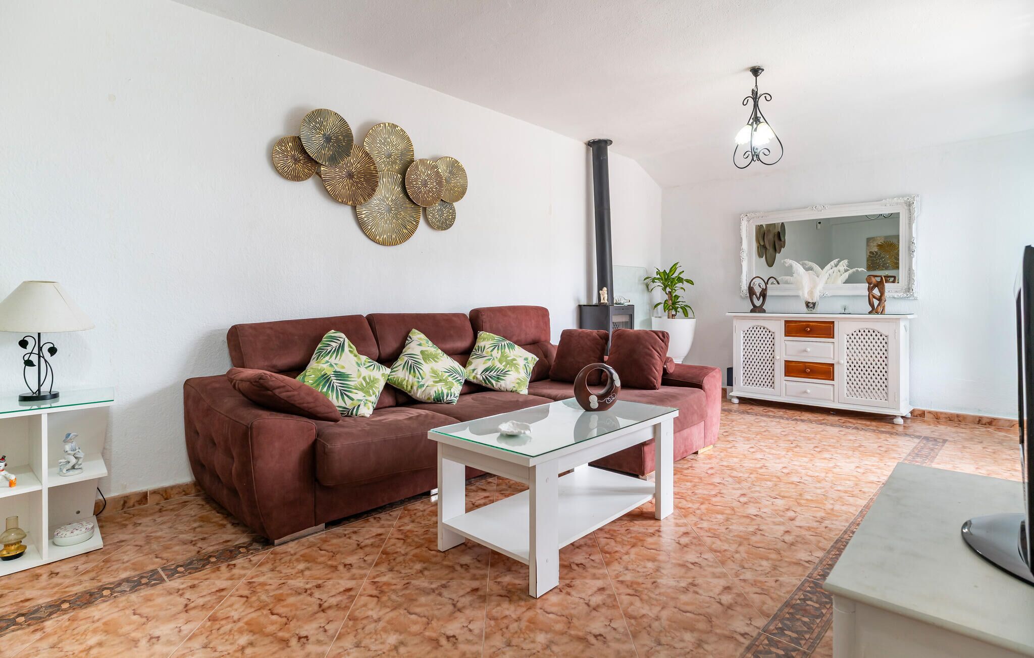 Un salon avec un canapé marron, une table basse en verre, un meuble blanc et un élément décoratif mural.