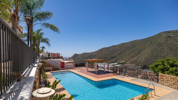 A rectangular swimming pool with a tiled deck, surrounded by a stone wall and a metal fence. - Alba de la Luna Apartment (Albuñol)