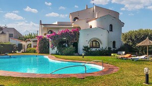 Ein großer Pool mit umgebender Rasenfläche und einem weißen Gebäude mit Bogenfenstern und einem Turm.