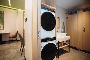 A hotel room with a washing machine, a sink, and a table with chairs.