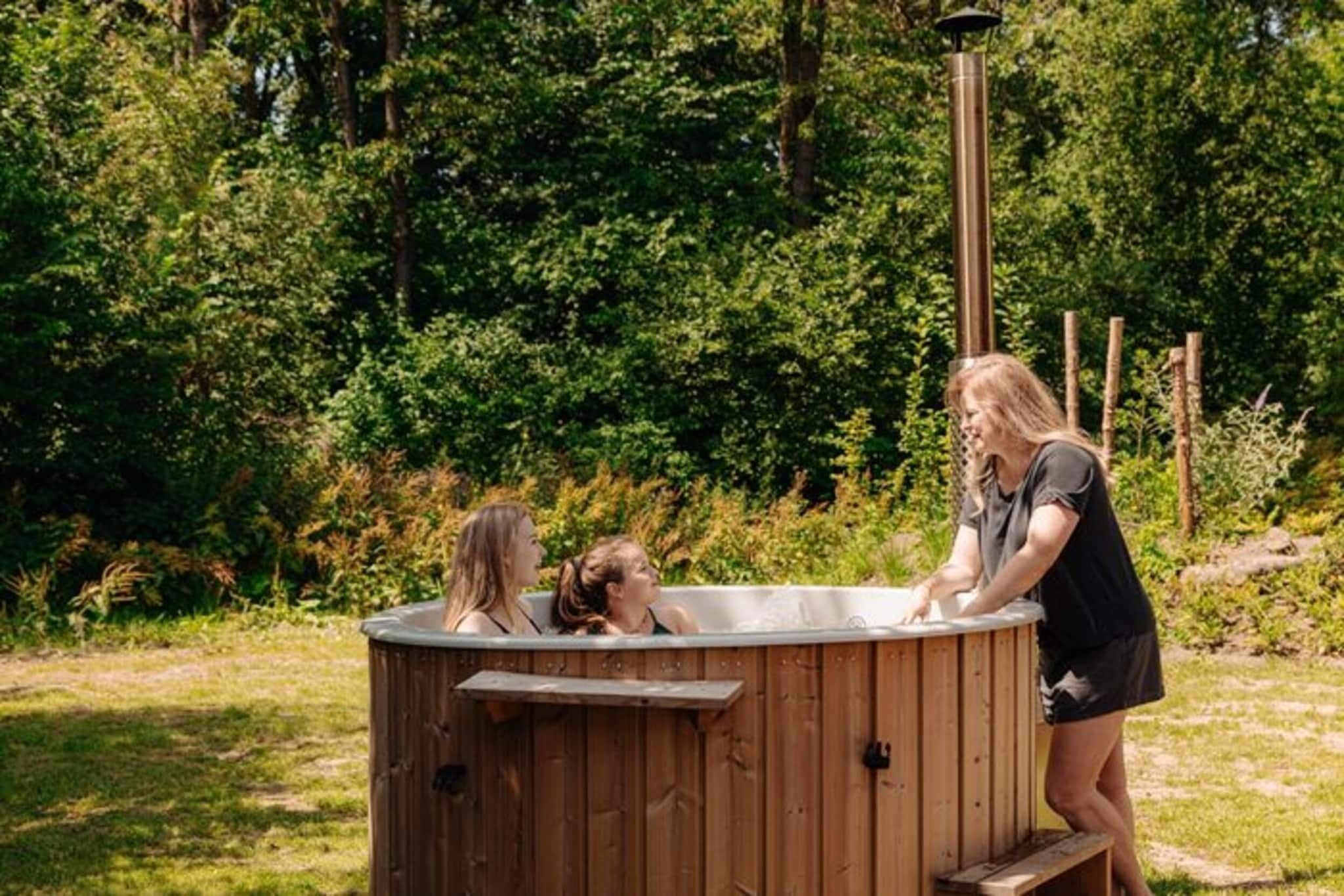 Un jacuzzi de madera en un jardín con abundante vegetación al fondo.