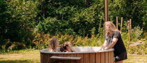 Un jacuzzi de madera en un jardín con abundante vegetación al fondo.