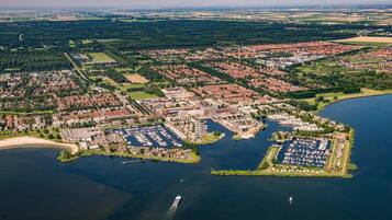 Luchtbeeld van een kuststad met een jachthaven, woonwijken en windturbines op de achtergrond.