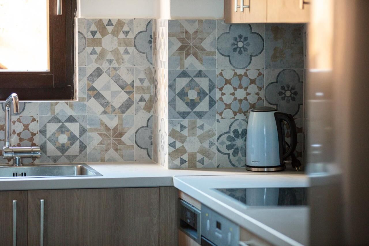 A kitchen with a sink, a kettle, and patterned tiles.