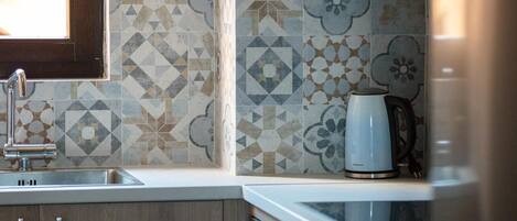A kitchen with a sink, a kettle, and patterned tiles.