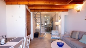 A modern living room with a wooden ceiling, a spiral staircase, a sofa, a coffee table, and a patterned armchair. - Fortezza Sea Breeze Anne-2BR with view (Rethymno)