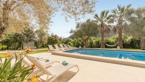 Un espace piscine avec des chaises longues, une piscine à l’eau d’un bleu limpide et une végétation luxuriante tout autour.