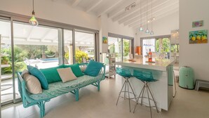 Une cuisine moderne avec un coin bar, un canapé aux coussins turquoise et une vue sur l’extérieur.