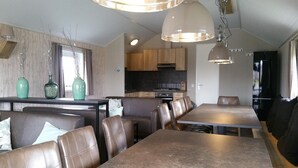 Een moderne keuken met houten kastjes, een zwart aanrecht en een inbouwoven. Er is een eethoek met bruine lederen stoelen en een lange tafel.