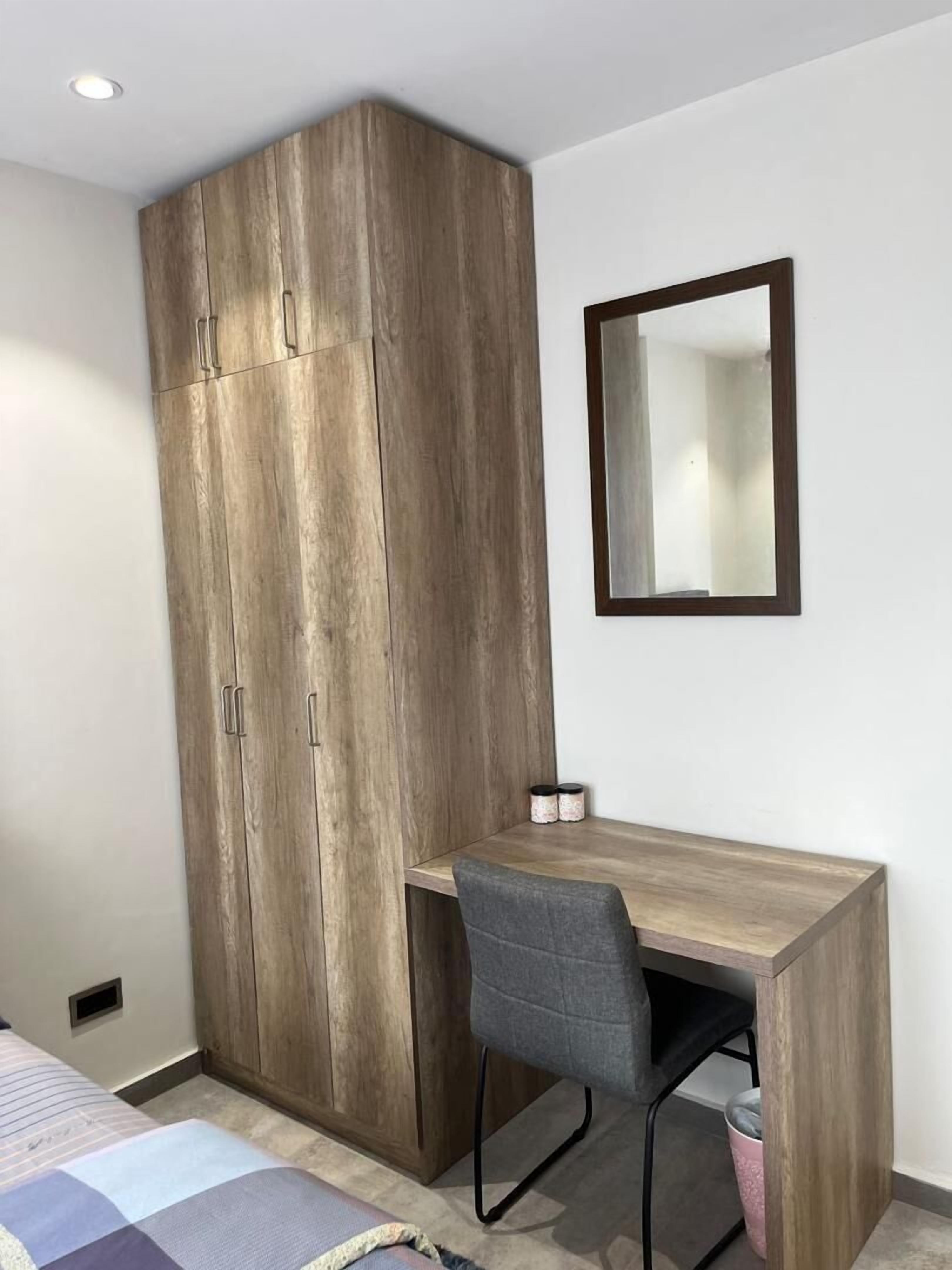 A bedroom with a wooden wardrobe, a desk, and a chair.