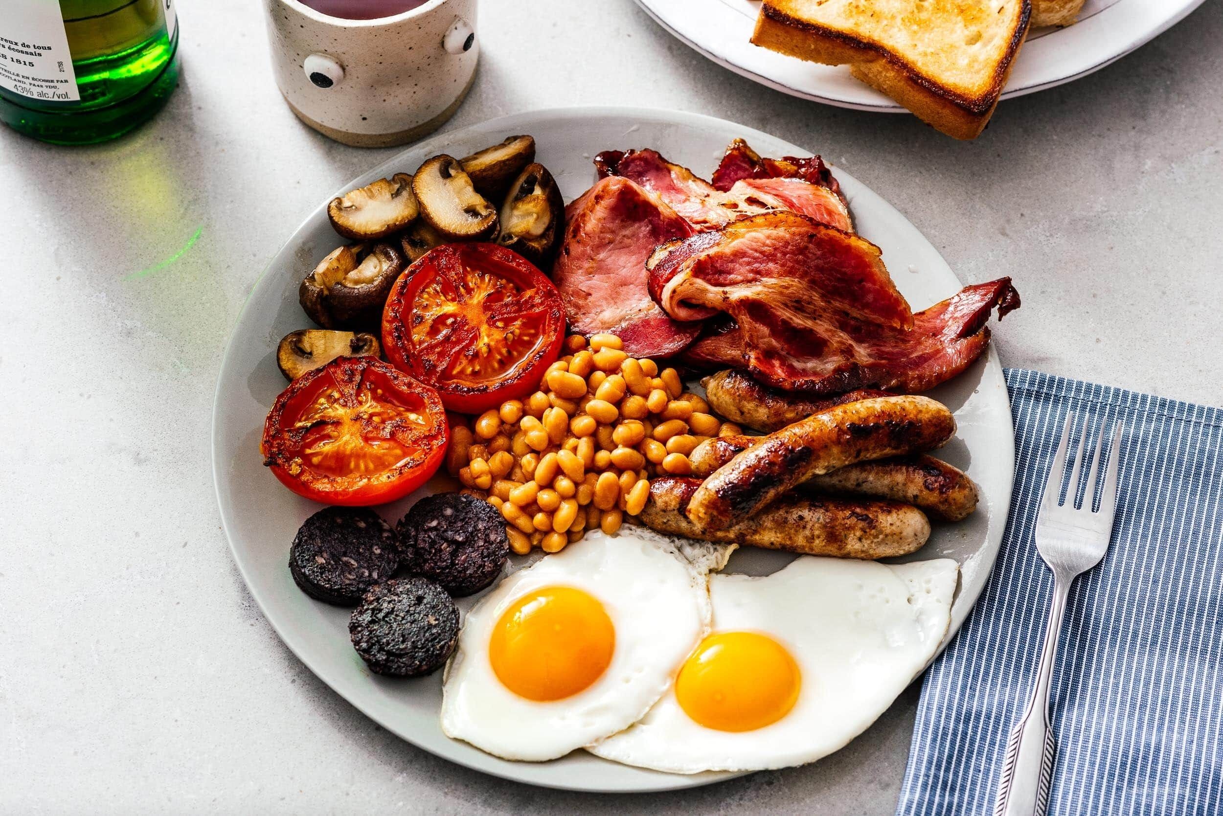 A plate of breakfast food including eggs, sausages, bacon, tomatoes, beans, and mushrooms.