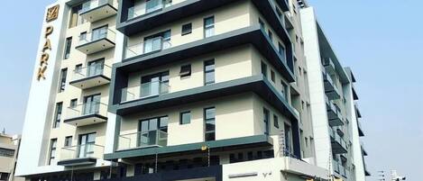 A multi-story building with a prominent 'PARK' sign, featuring balconies, a covered entrance, and a gated driveway.