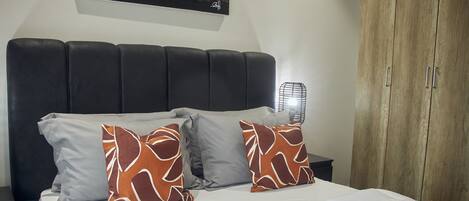 A bed with a black headboard, two pillows with a leaf pattern, a white bedspread, and a nightstand with a lamp.