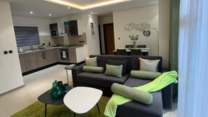 A modern living room with a sectional sofa, a coffee table, and a green rug. - Spring Properties - Hotel Apartments (Accra)