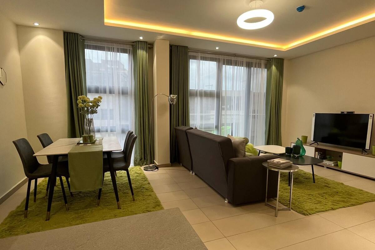 A modern living room with a dining area, a sofa, a TV, and a green rug.