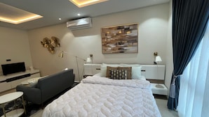 A modern hotel room with a bed, bedside tables, a desk, a chair, a TV, and decorative wall art. - Spring Properties - Hotel Apartments (Accra)