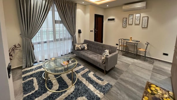 A modern living room with a sofa, coffee table, and a dining area with chairs. - Spring Properties - Hotel Apartments (Accra)