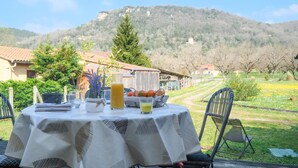Ein Essplatz im Freien mit Tischdecke, einer Karaffe, einem Glas Saft und einem Brotkorb.
