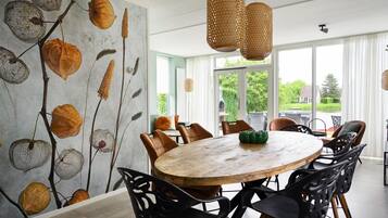 Een eetruimte met een ronde houten tafel, zwarte stoelen en een muurschildering van herfstbladeren.