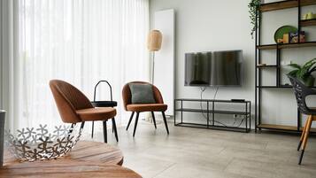 Een moderne woonkamer met een televisie, twee fauteuils, een console tafel en een boekenkast.
