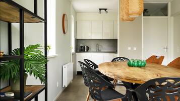 Een moderne keuken met witte kastjes, een houten eettafel, zwarte stoelen en een hangende rieten lamp.
