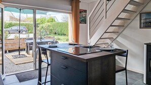 Eine moderne Küche mit Kochinsel, einem Essbereich mit Tisch und Stühlen sowie Blick auf Garten und geparktes Auto durch Glastüren.
