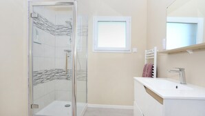 Un baño moderno con ducha envuelta en cristal, un lavamanos blanco y un espejo encima.
