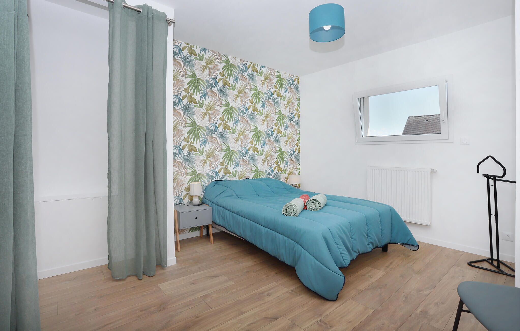 Une chambre à coucher avec un lit, une fenêtre, un radiateur, une lampe et un rideau.