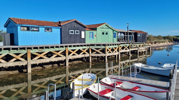 Une jetée en bois, bordée de bâtiments aux couleurs vives et où sont amarrés des bateaux à son extrémité.