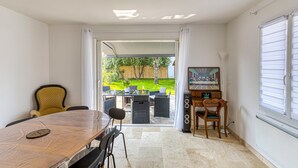 Une pièce comprenant une table à manger, des chaises, un téléviseur et donnant sur un jardin.