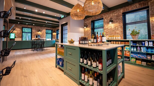 A bar area with wooden floors, green bar stools, and shelves stocked with bottles.