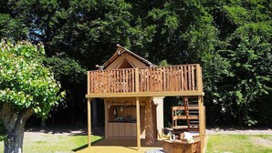 A wooden cabin with a balcony, a kitchen area, and a seating area with a table and chairs.