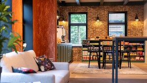 A cozy living area with a sofa, a coffee table, and a dining table with chairs. There is a brick wall and a window with blinds.