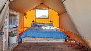 A tent with a bed, a window, and a shelf with decorative items.