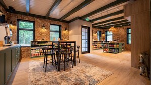 A cozy restaurant with exposed brick walls, wooden beams, and a rustic interior. There is a bar area with stools and shelves stocked with snacks.