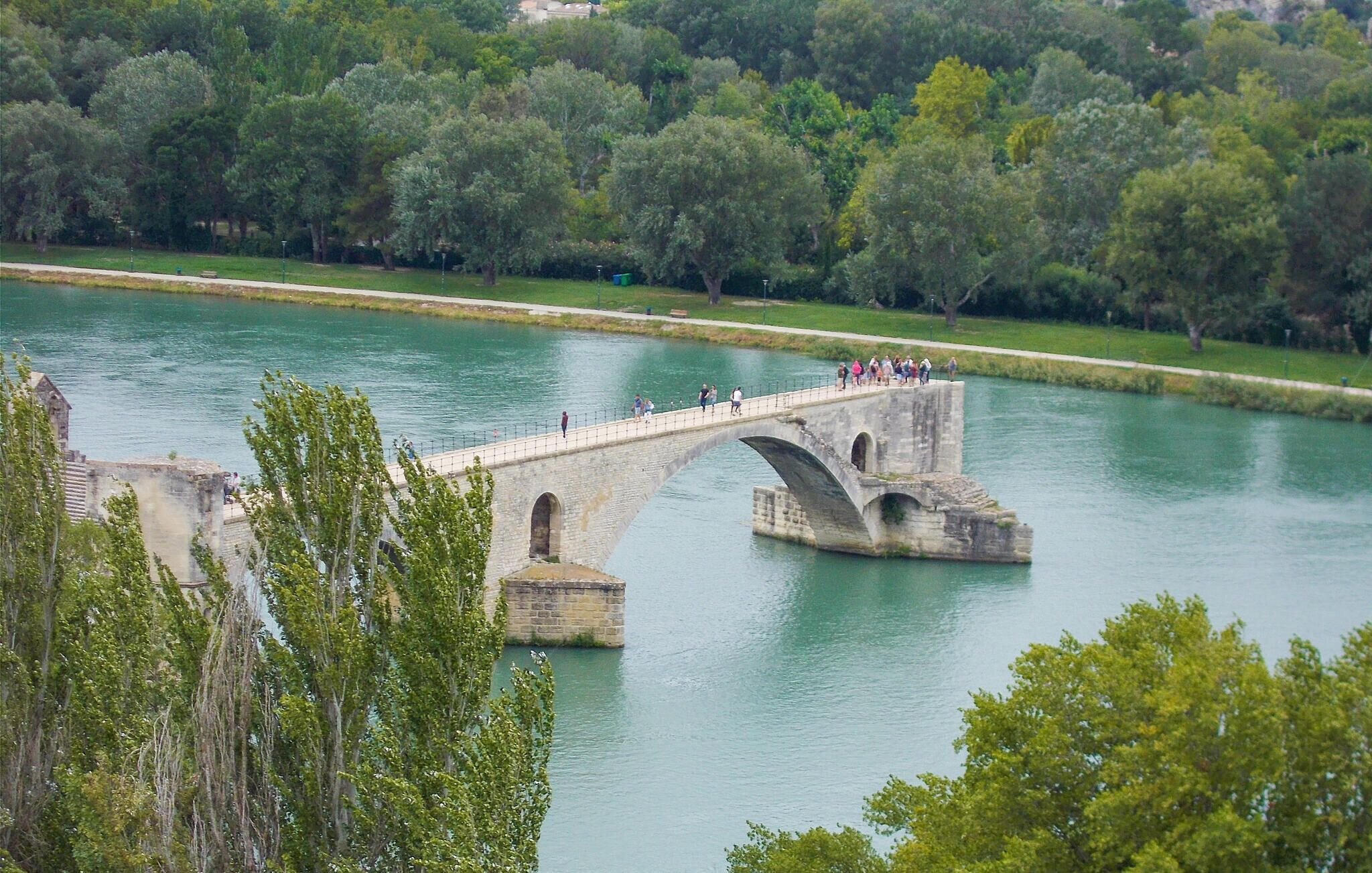 A stone bridge over a calm river with people walking on it.