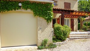 A building with a closed garage door, a covered patio area, and a stone wall with greenery. - Stunning home in Vedène (Vedène)