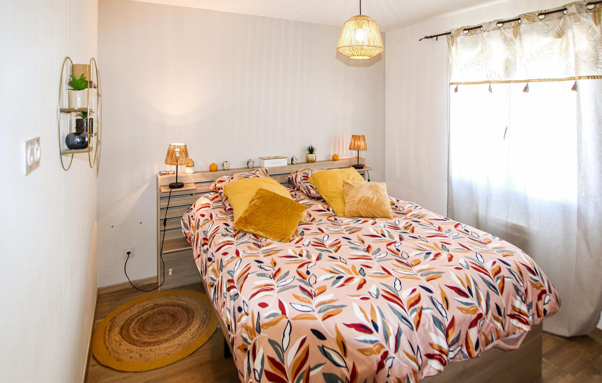 Un dormitorio con una cama, lámparas de noche, un estante en la pared con plantas y una ventana con cortinas.