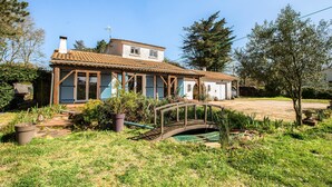 Ein zweistöckiges Haus mit Ziegeldach, einer Laube und einer kleinen Brücke über einem Garten.
