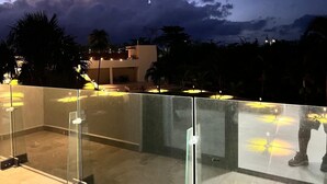A glass-enclosed outdoor area with a view of a building and palm trees. - Modern studio in a beachfront building (Cozumel)