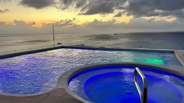 A pool with a view of the ocean at sunset. - Modern studio in a beachfront building (Cozumel)