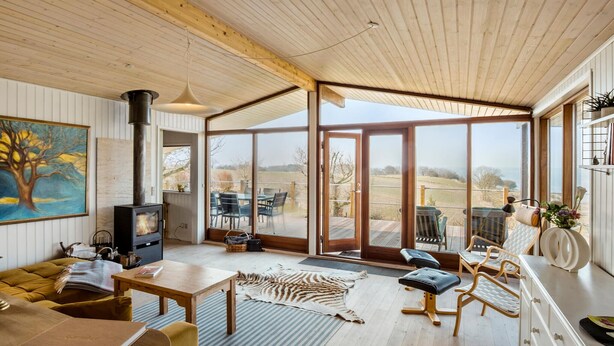Een ruime woonkamer met een groot houten plafond, een open haard en uitzicht op de omgeving door middel van grote glazen deuren.
