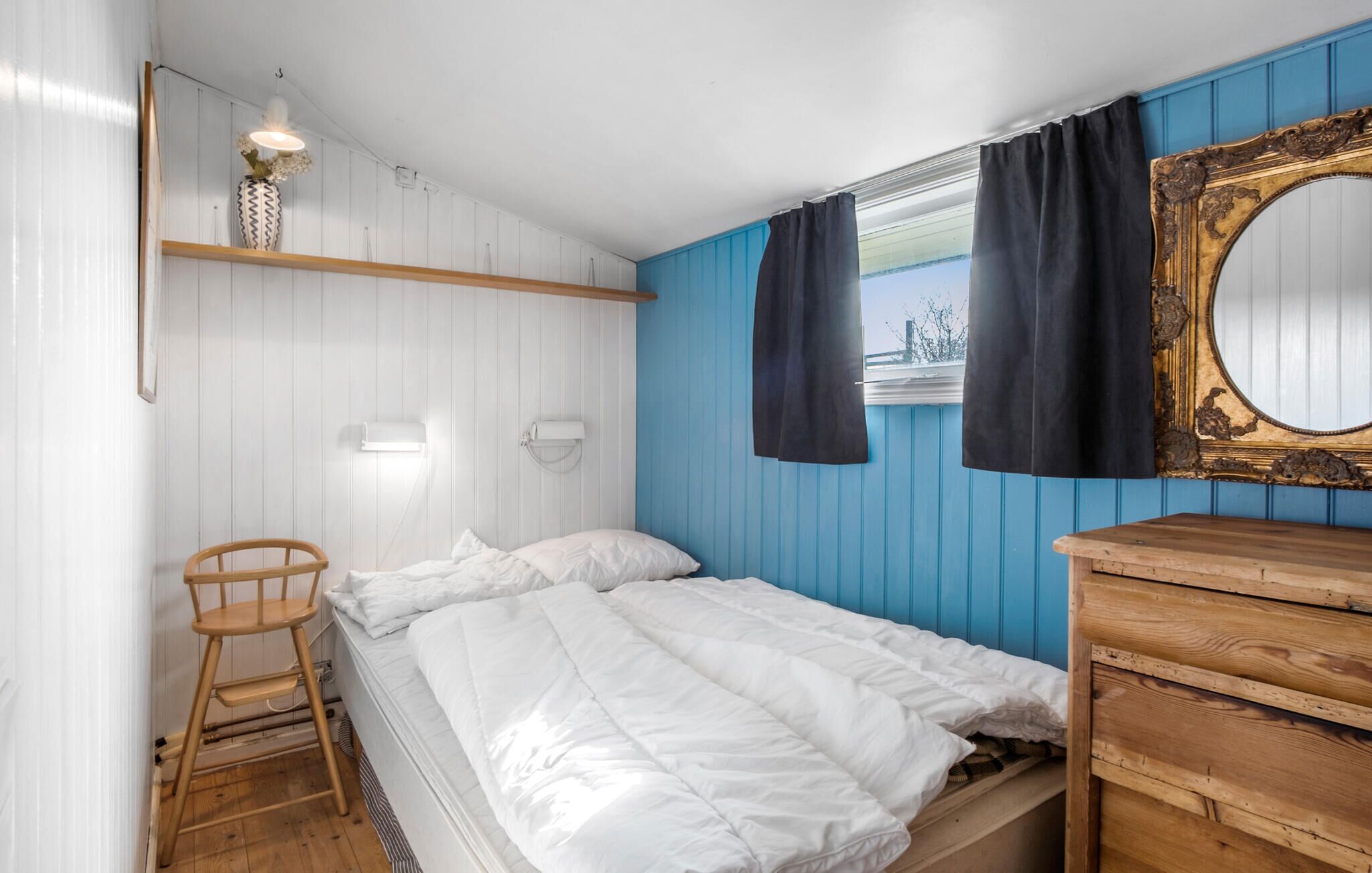 A bedroom with a bed, a wooden chair, a dresser, a mirror, and a window with curtains.
