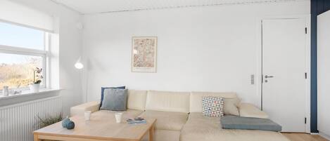 Una sala de estar moderna con un sofá color beige, una mesa de centro de madera e impresión botánica enmarcada en la pared.